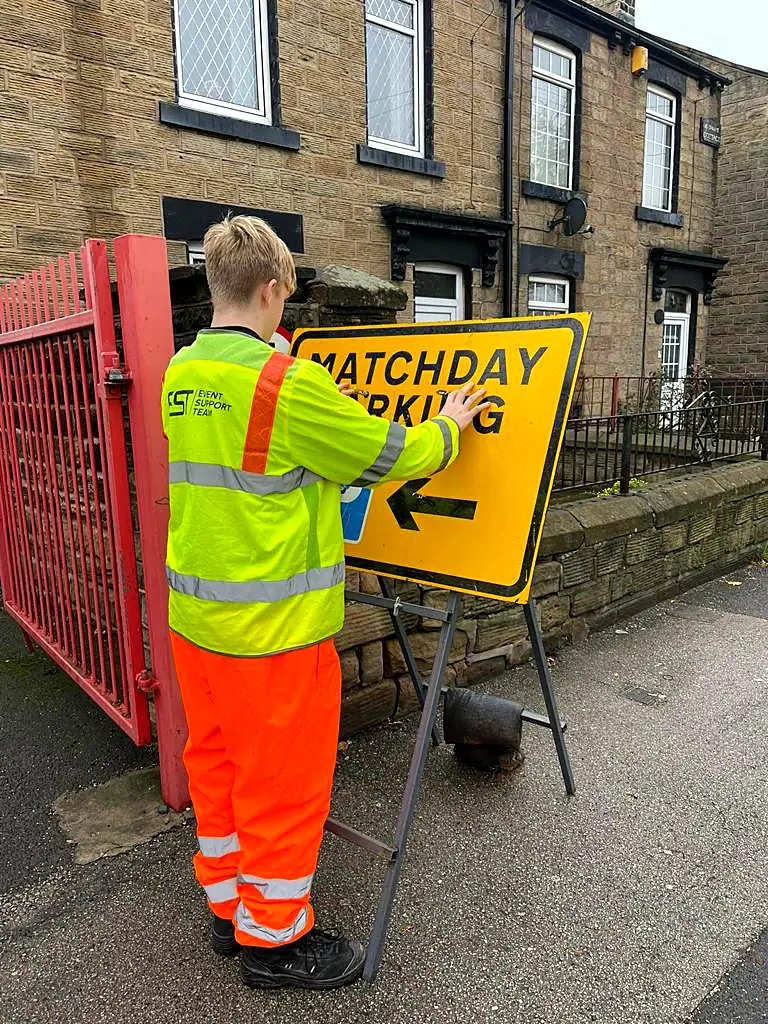 An EST operative fixing a Matchday Parking arrow sign by a row of terraced houses